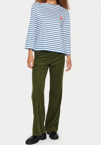 Pasiasta koszula z długim rękawem w niebiesko-białe paski, z haftowanym detalem. Połączona z oliwkowymi spodniami z sztruksu o szerokich nogawkach i czarnymi butami.