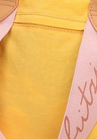 Interno giallo in cotone con una texture morbida, accentuato da spalline rosa chiaro con un sottile dettaglio del logo.