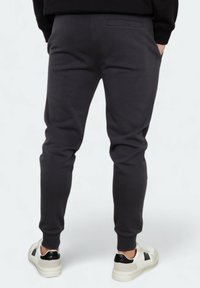 Dunkelgraue Jogginghosen aus weichem Stoff mit schmal zulaufenden Beinen, elastischem Bund und einer Detailtasche auf der Rückseite, kombiniert mit weißen Sneakers mit niedrigem Schaft.