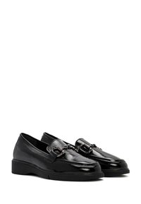 Zwarte gepatineerde leren loafers met een laag plateau, voorzien van een kettingaccent over de voorkant. Gladde textuur en afgeronde neusontwerp.