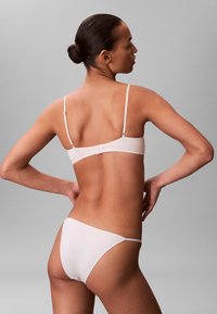 Lichtroze, naadloze bh- en bikiniset met dunne verstelbare bandjes en subtiele sluiting, gemaakt van zacht, glad materiaal.