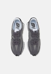 Grå sneakers med mesh- och mockamaterial, med runda snören, en distinkt form och ett svart accentband på sidan.