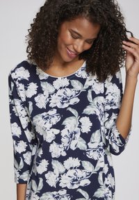 Top floreale navy con maniche a tre quarti e scollatura rotonda, con motivi di fiori bianchi e azzurri su un tessuto morbido.