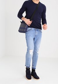Borsa a tracolla navy con strisce orizzontali, abbinata a una camicia a maniche lunghe aderente, jeans chiari strappati e scarpe scure in suede.