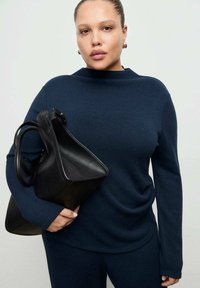 Top blu navy a maniche lunghe in tessuto morbido, abbinato a una borsa in pelle nera con design strutturato e doppi manici.