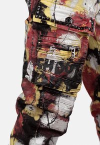 Pantalons cargo avec un motif éclaboussé vif en rouge, jaune et noir. Accentué de clous noirs et d'une poche zippée en métal argenté.