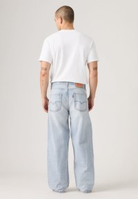 Light blue denim jeans with a loose fit, featuring back pockets and a classic leather tag. Paired with a plain white t-shirt.