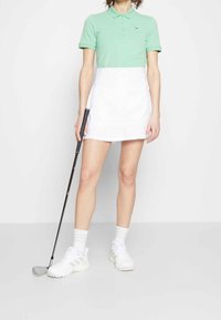 Golf outfit featuring a mint green polo, white skort, and white sneakers. The polo has a button placket, and the skort is above the knee.