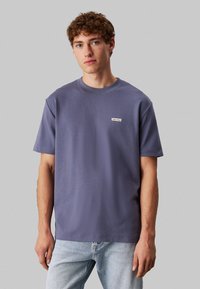 T-shirt crew neck viola in cotone con maniche corte, dotato di una piccola patch con il logo Calvin Klein sulla parte sinistra del petto. Vestibilità classica.