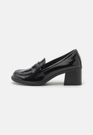 Sort laklæder loafers med blokhæl, rund tå og remdetalje, vist i sideprofil på hvid baggrund.