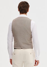 Brązowa kamizelka w wzory o teksturowanym wykończeniu, noszona na białej koszuli. Posiada dopasowany krój i gładki tył bez widocznych zapięć.