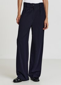 Pantaloni a righe navy con vita alta, frontale plissettato e chiusura con bottone, realizzati in tessuto liscio. Vestibilità ampia e gambe leggermente svasate.