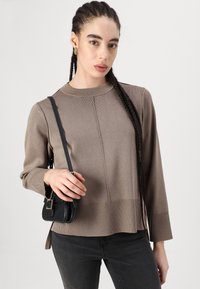 Brązowy sweter prążkowany z okrągłym dekoltem, długimi rękawami i bocznymi rozcięciami, w zestawieniu z małą czarną torebką na ramię.