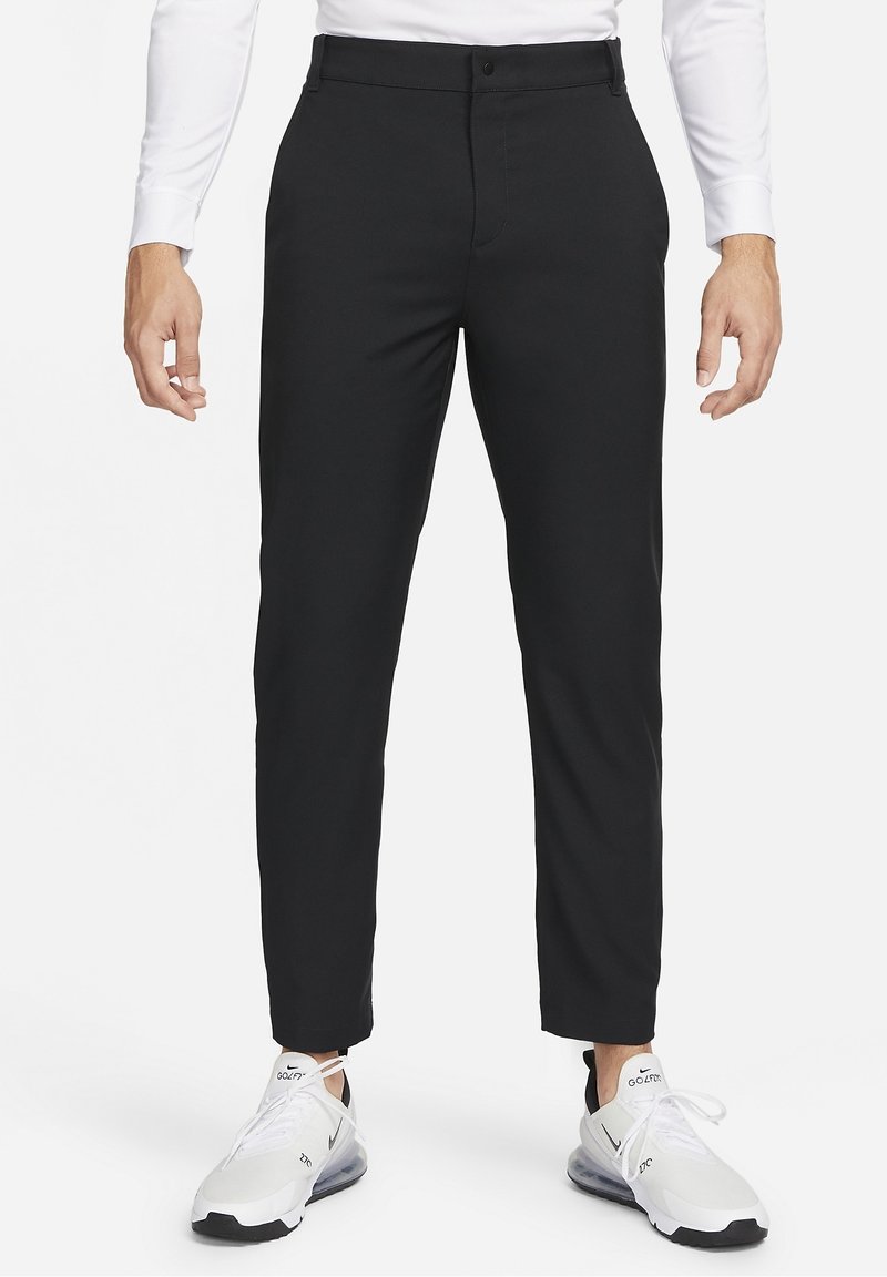 Homme portant un pantalon noir slim, une chemise blanche et des baskets blanches Nike Air Max 270, debout, les bras détendus le long du corps.