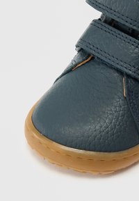 Pantof din piele albastru închis cu o suprafață texturată, prevăzut cu două curele cu velcro și talpă din cauciuc de tip gumă. Design cu vârf rotunjit.