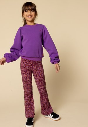 Paarse sweatshirt met opgezette mouwen en een klein logo, gecombineerd met gestreepte flared broeken in paars en oranje. Gestyled met zwarte sneakers.