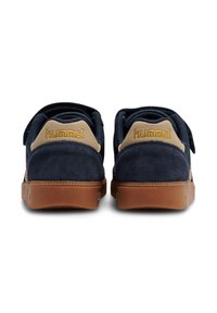 Widok z tyłu granatowych zamszowych tenisówek z beżowym akcentem logo, grubą gumową podeszwą i regulowanym paskiem do zapięcia.