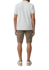 Witte katoenen polo met korte mouwen, gecombineerd met bruine shorts tot de knie. Witte sneakers met lichte grijze accenten maken de outfit compleet.