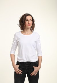 Weißes Langarmshirt mit rundem Halsausschnitt, kombiniert mit hochtaillierten schwarzen Jeans mit Knopfleiste und zwei vorderen Taschen.