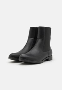 Mustad nahast pahkluu saapad elastsete külgpaneelidega, ümar toe ja madala virnastatud kanna külge. Sile tekstuur koos minimalistikuga disainiga.