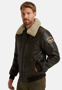 Brun läder bomberjacka med en beige sherlingskrage, ribbade ärmslut och fickor, med orange sömmar och broderade logodetaljer.