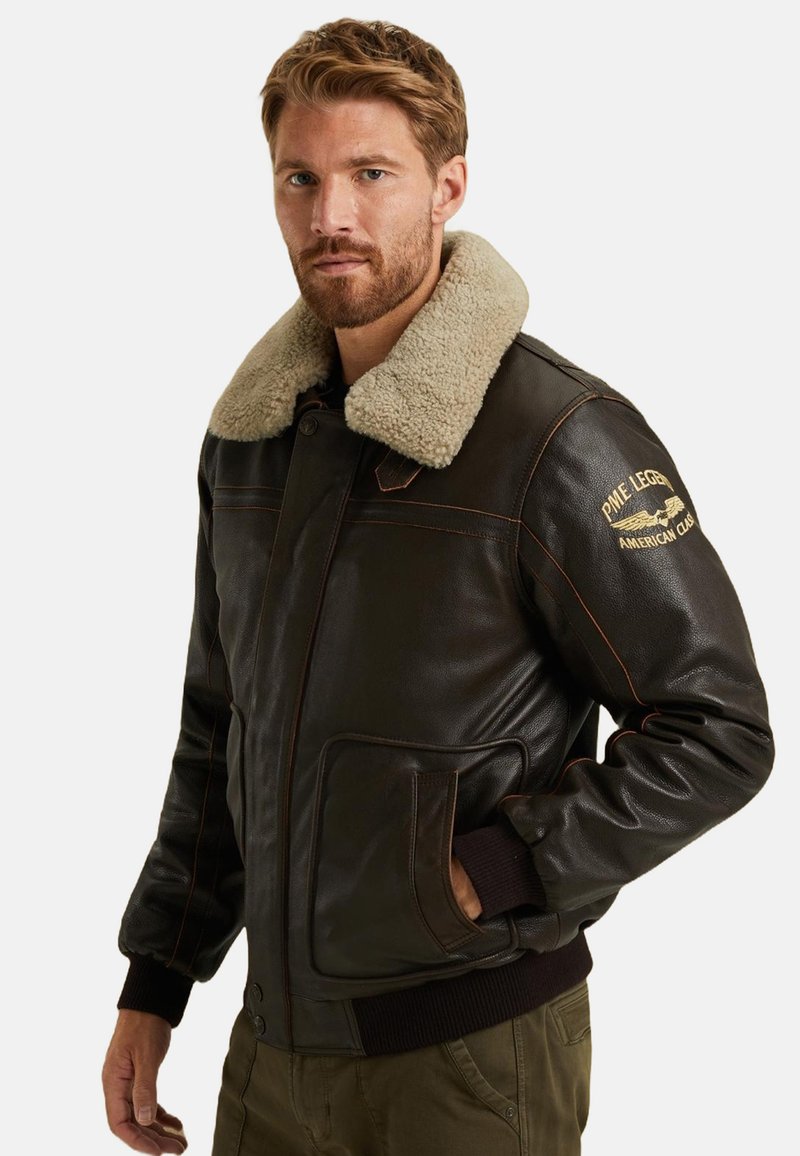 Brun läder bomberjacka med en beige sherlingskrage, ribbade ärmslut och fickor, med orange sömmar och broderade logodetaljer.