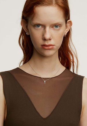 Vestido marrón con pliegues y un panel de seda en forma de V. La modelo lleva un delicado collar de plata con un pequeño colgante. Ojos azul brillante y cabello rojo.