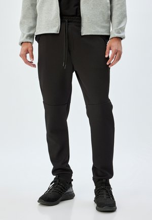 Sorte sweatpants med en tætsiddende pasform, elastisk talje og snor. Lavet af et glat, tekstureret stof med sømmede detaljer og sidelommer.