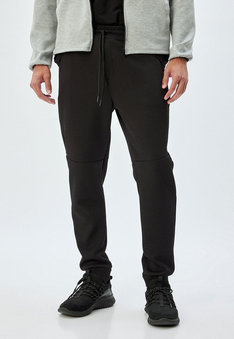 Sorte sweatpants med en tætsiddende pasform, elastisk talje og snor. Lavet af et glat, tekstureret stof med sømmede detaljer og sidelommer.