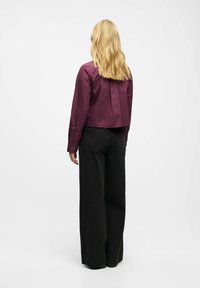 Kort, blommefarvet bomuldsskjorte med lange ærmer, plissédetalje på ryggen, kombineret med sort, høj taljet bukser med vide ben.