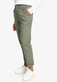 Pantalon vert en mélange de coton, coupe décontractée, doté de poches latérales, d’un ourlet retroussé et d’une ceinture avec fermeture élastiquée et bouton.