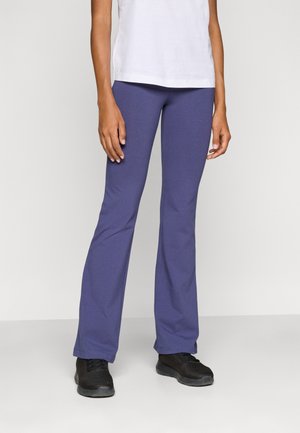 Leggings viola a campana in tessuto morbido e elasticizzato, abbinati a scarpe sportive nere. L'outfit è completato da una semplice t-shirt bianca sulla parte superiore.