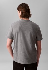 Γκρι μπλουζάκι με κοντά μανίκια και στρογγυλή λαιμόκοψη. Μαλακό ύφασμα, ελαφρώς χαλαρή εφαρμογή και λεία υφή. Μινιμαλιστικός σχεδιασμός χωρίς εμφανή λογότυπα.