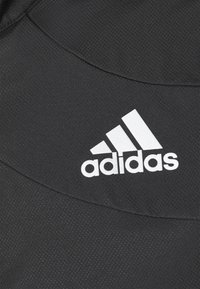 Gros plan sur un tissu noir texturé avec le logo Adidas blanc comprenant trois bandes et le nom de la marque.