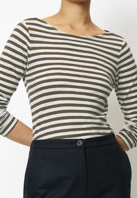 Randig långärmad topp i brunt och vitt, med vid halsringning och figurnära design, i kombination med mörka skräddarsydda byxor.