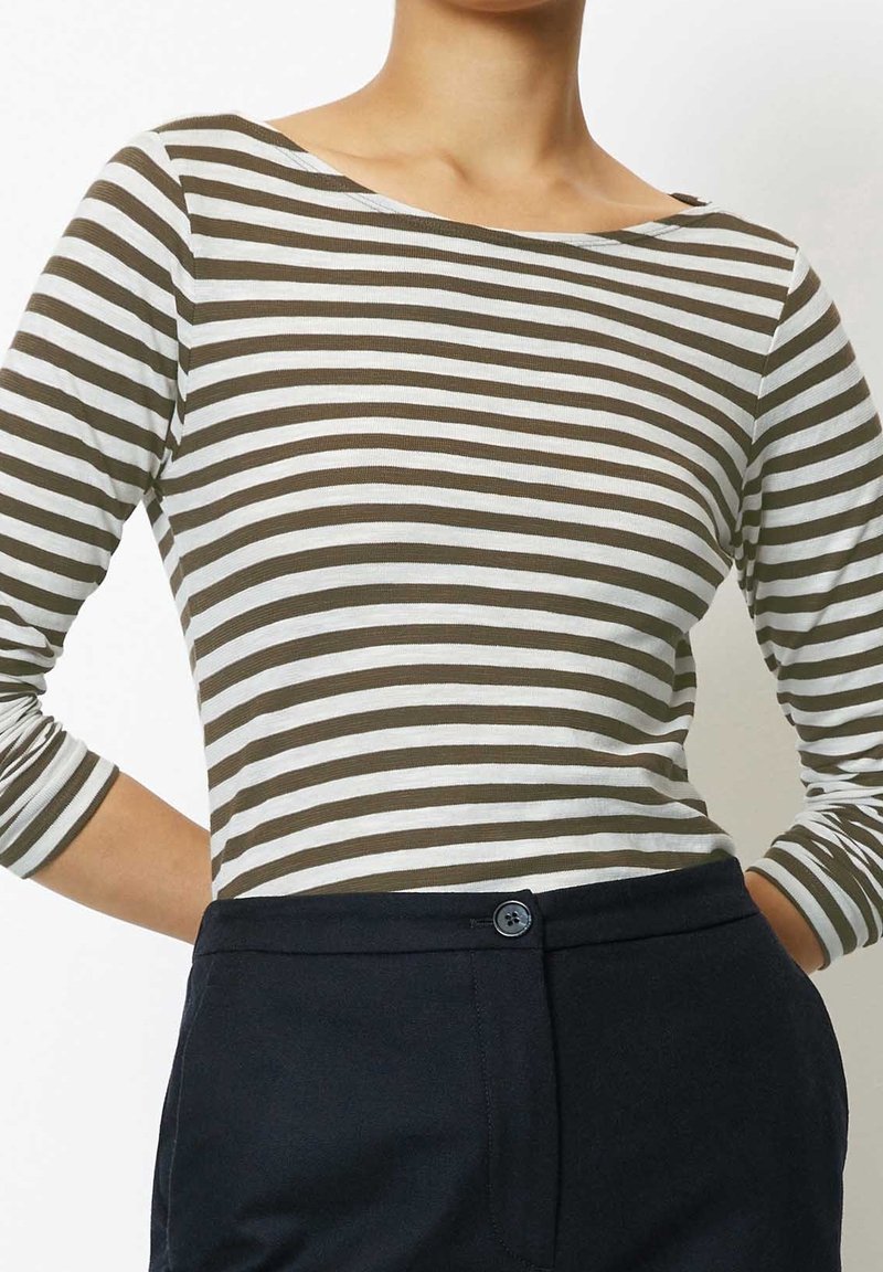 Randig långärmad topp i brunt och vitt, med vid halsringning och figurnära design, i kombination med mörka skräddarsydda byxor.