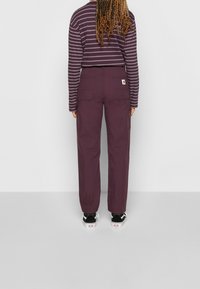 Cargo pants in deep purple cotton, featuring side pockets, a relaxed fit, and a patch label. Striped long-sleeve top in dark purple and light lilac.