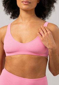 Rosa sömlös bralette med breda axelremmar och rundad halsringning. Tillverkad av mjukt, texturerat material, har den en slät, odekorerad design.