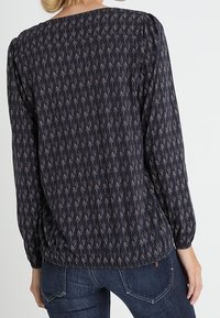 Marinblus med geometriskt mönster i ljusa färger, rund halsringning, långa puffärmar och rynkade detaljer i nederkant.