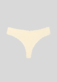Culotte string sans couture de couleur crème avec bords festonnés sur un fond gris clair.