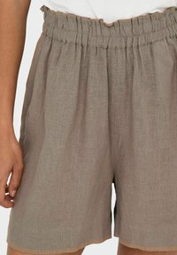 Pantaloni corti di lino khaki con vita elastica, caratterizzati da una vestibilità rilassata e dettagli cuciti. La trama è morbida e leggermente texturizzata.