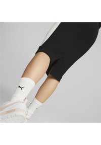 Pantaloni sportivi neri con aperture laterali, abbinati a calzettoni bianchi a coste con un logo nero e scarpe sportive chiare.