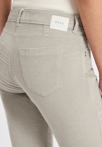 Lichtgrijze denim jeans met een zachte textuur, voorzien van een achterzak met flap en een merklabel bij de taille. Klassiek vijfzakkenontwerp.