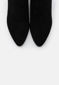 Czarne zamszowe botki na obcasie o szpiczastym nosku, charakteryzujące się gładką teksturą i eleganckim wzornictwem. Posiadają smukły obcas oraz otwarte boki zapewniające wentylację.