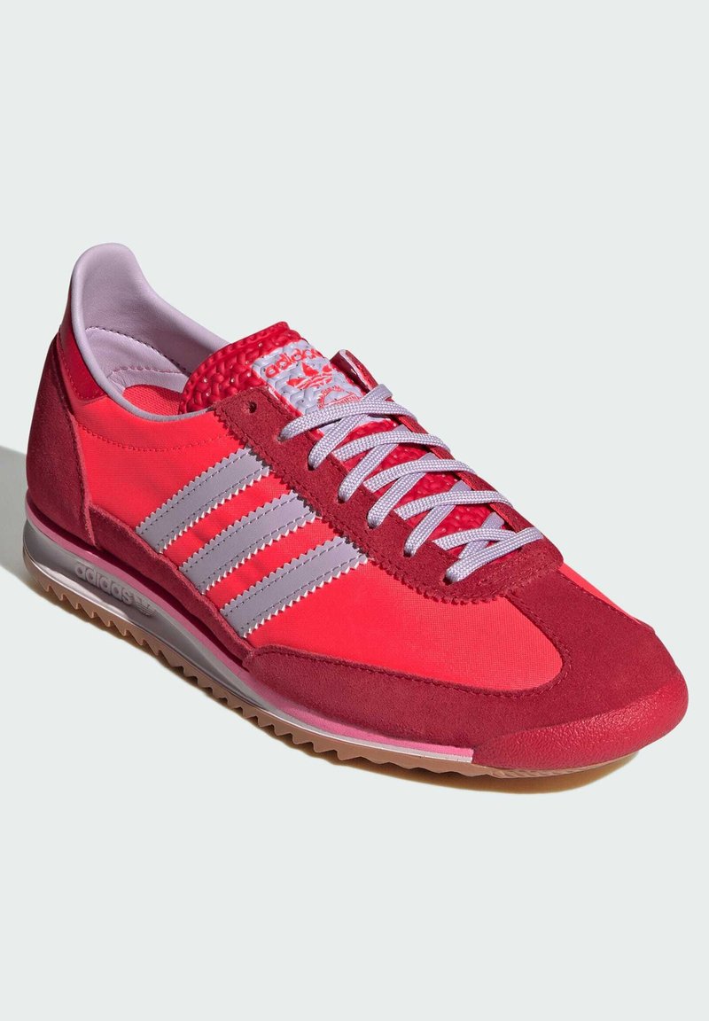 Zapatilla deportiva roja con parte superior de textil suave y acentos de ante, tres rayas grises y una suela de goma con un agarre texturizado.