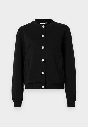 Veste noire avec un col rond, texture en chevrons et fermeture à boutons dorés. Possède des poches latérales et des poignets et un ourlet côtelés.