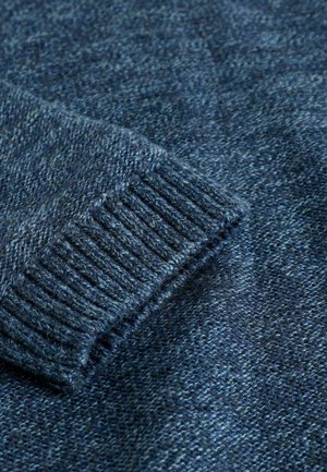 Mörkblå stickad tröja med ribbad mudd, texturerad tyg med blandade fibrer och en slät finish. Nära bild av ärmdetalj.