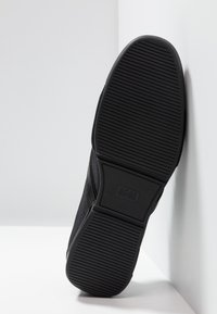 Czarne sneakersy z teksturowaną górną częścią z materiału, gumową podeszwą z żebrowanym wzorem i wytłoczonym logo marki na pięcie.