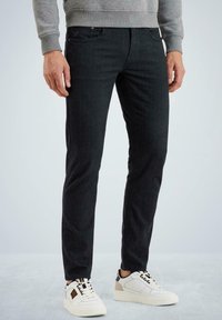 Jeans de mezclilla negra con corte ajustado, con cinco bolsillos y un sutil acabado texturizado, combinados con zapatillas blancas y negras.