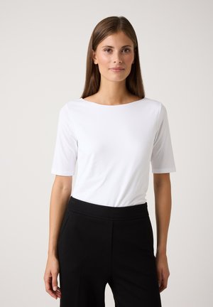 White short-sleeve top with a rounded neckline, paired with black pants. The fabric appears smooth with a minimalistic design and no patterns.